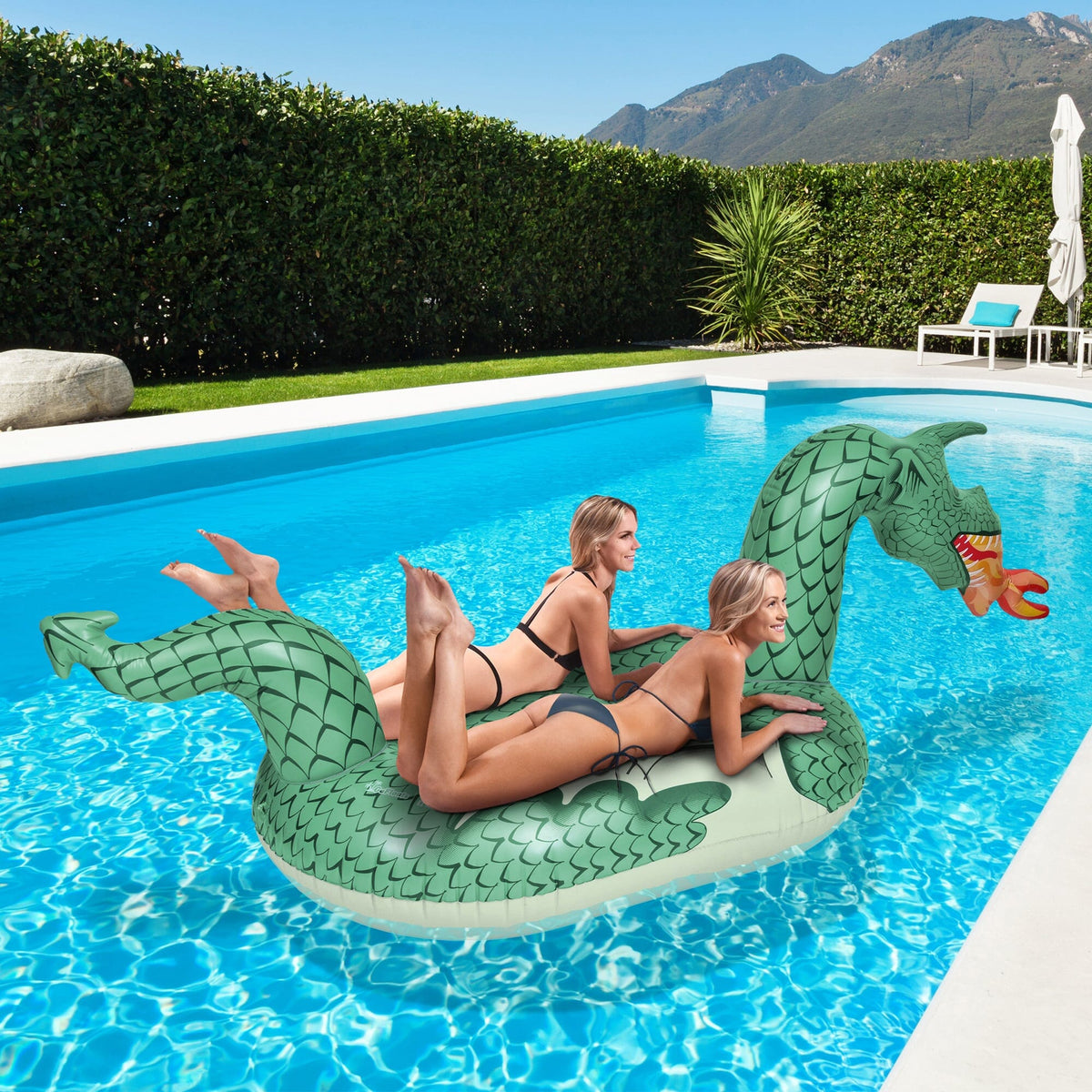 Two women lounging on a GoFloats giant Fire Dragon pool float in a backyard swimming pool