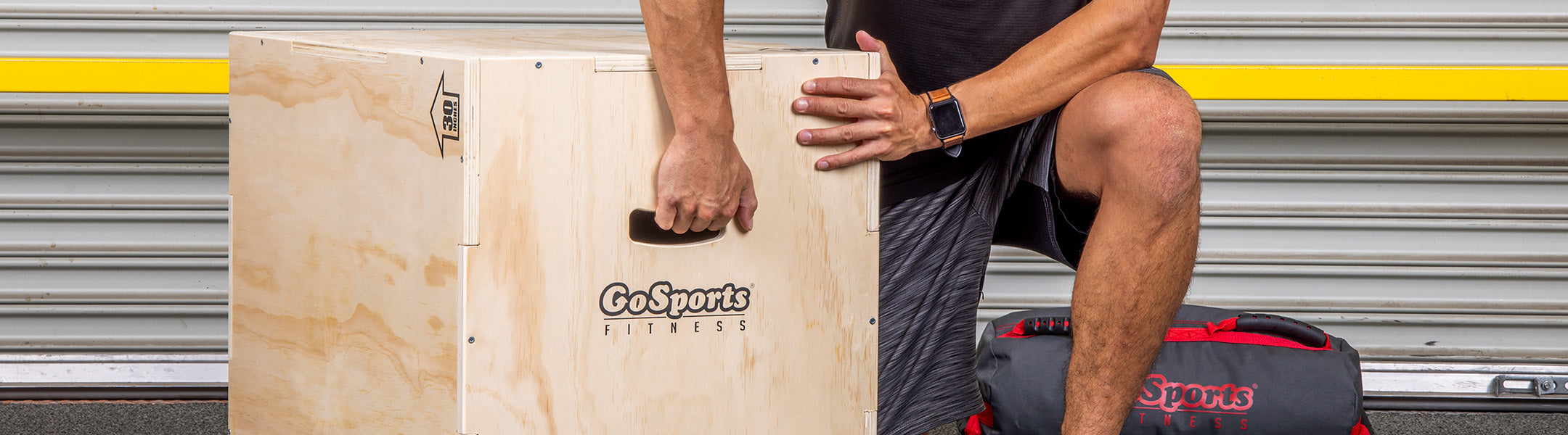 Person holding a wooden box with 'GoSports' branding in front of a garage door.