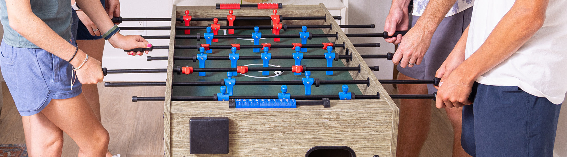 People playing foosball with a focus on the table and players' hands.