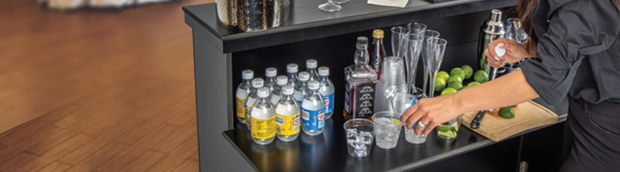 Bar setup with bottles, glasses, and a person preparing drinks.