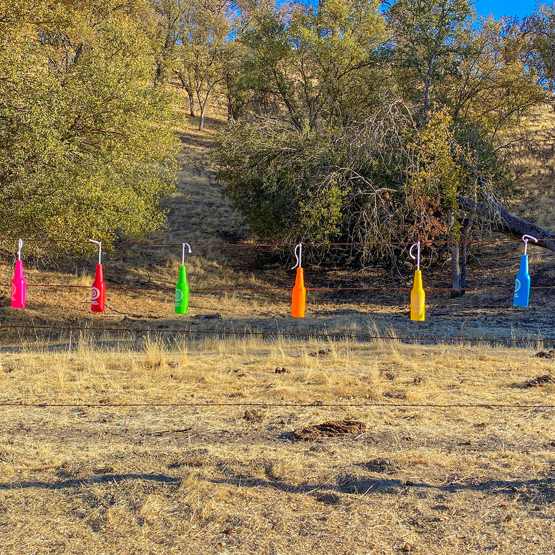 Colorful plastic bottles attached to sticks in a grassy field with trees in the background