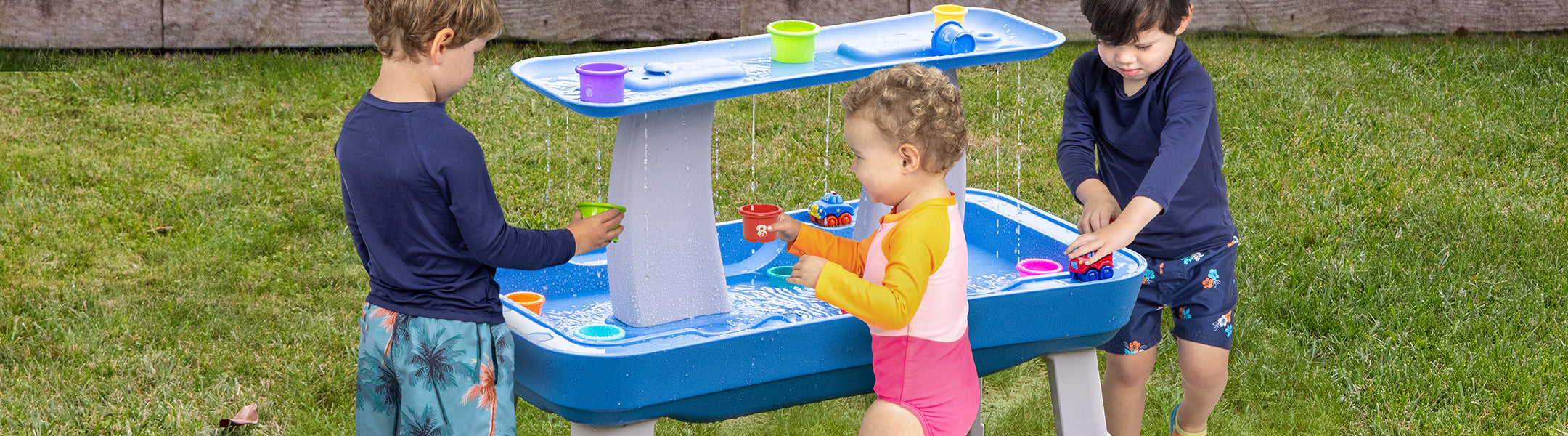 Children playing with a water table outdoors on a grassy area.
