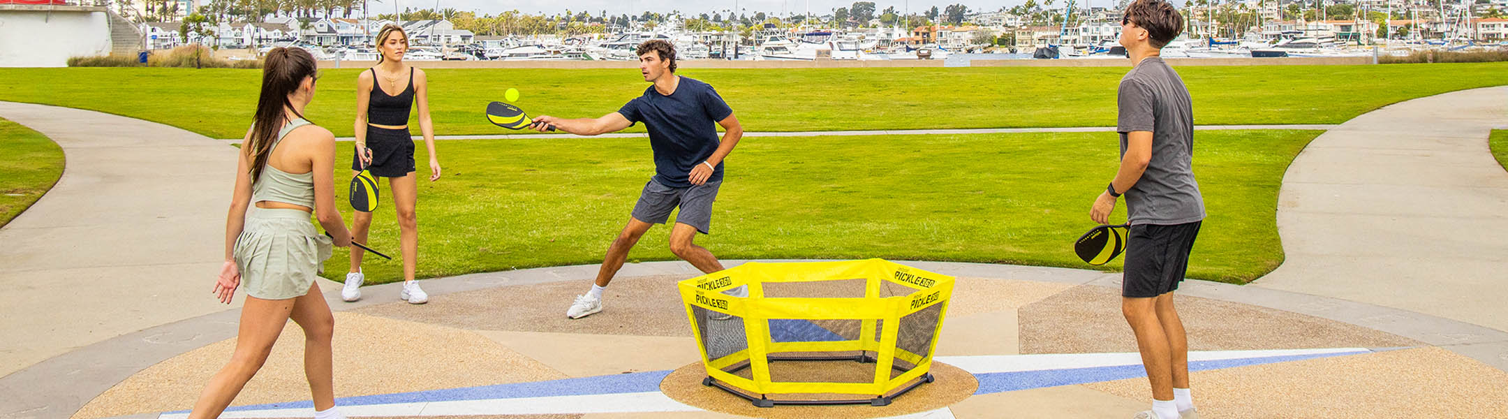 Four people playing pickleball on a grass court with a yellow net.
