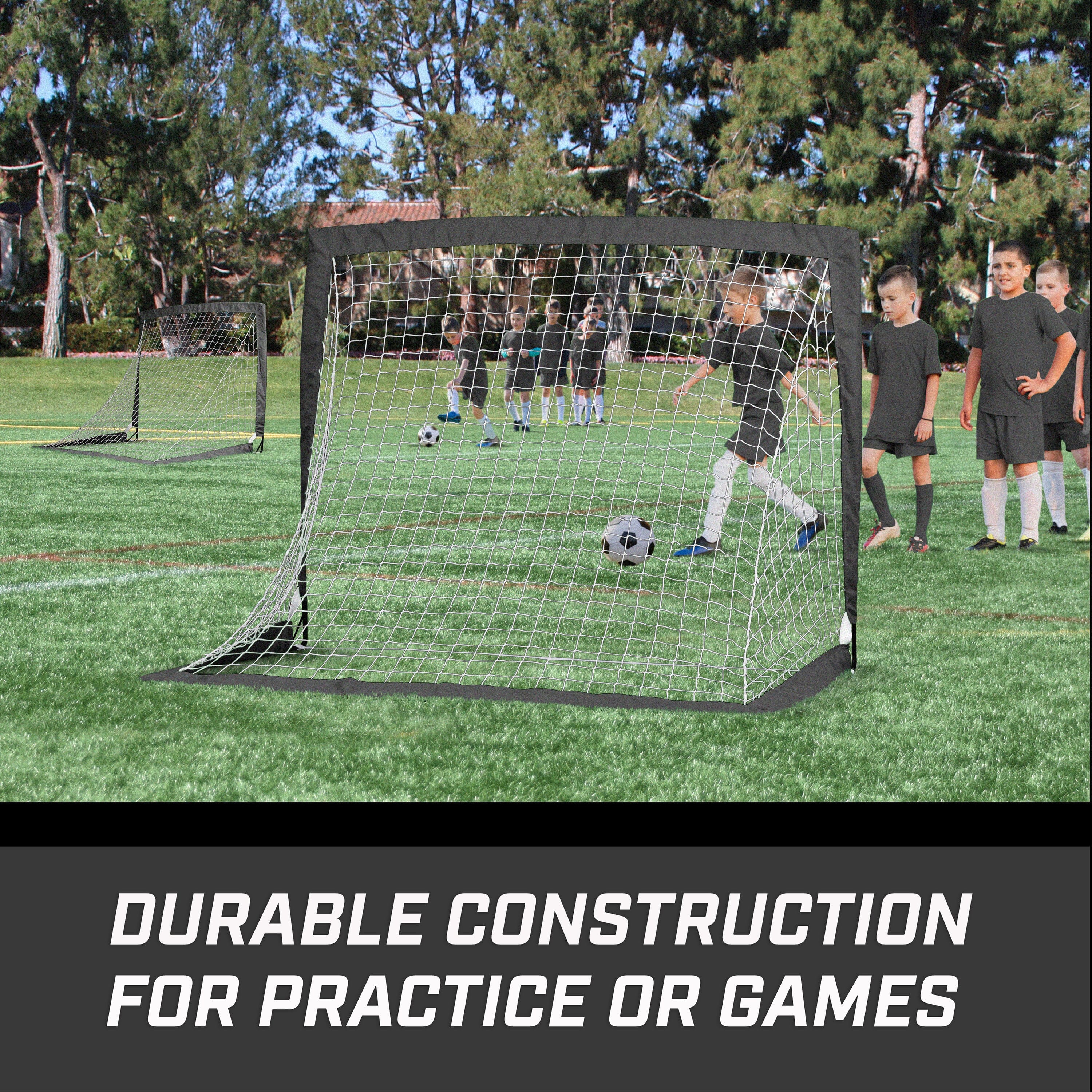 Children playing soccer on a field with a portable goal, surrounded by trees.