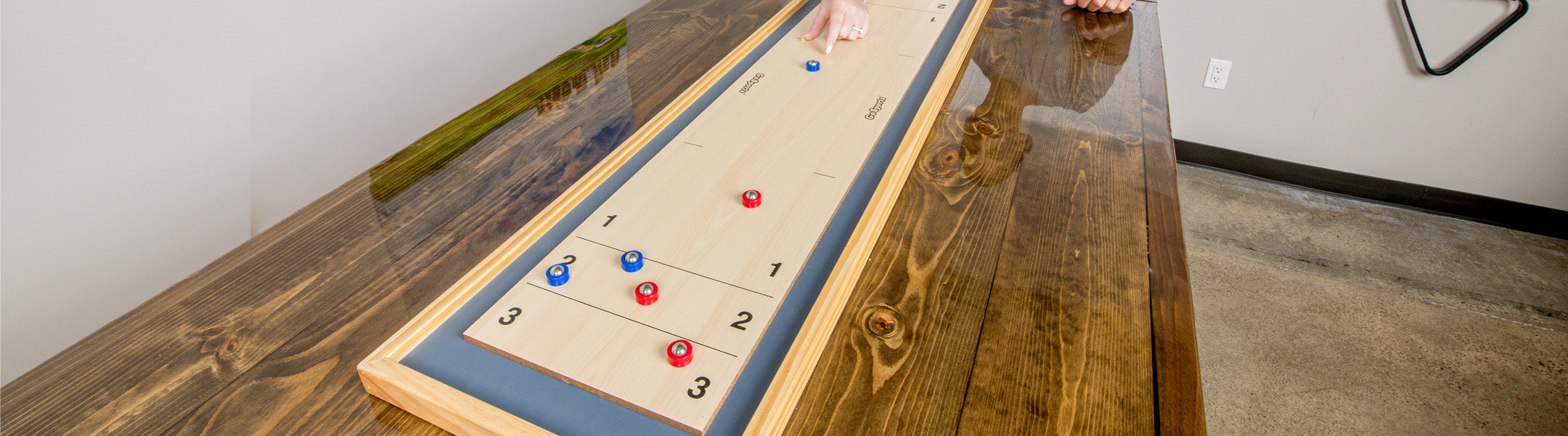 Wooden shuffleboard table with red and blue pucks on a wooden floor.