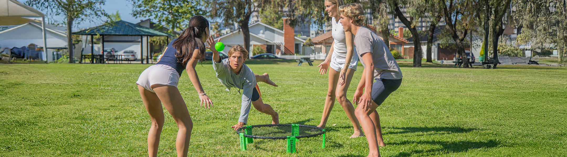 people playing slammo round net on a grassy ground