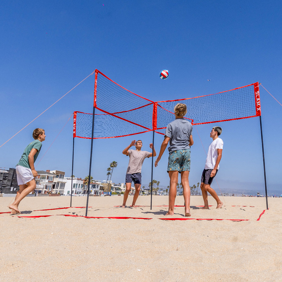 Four people playing beach volleyball on a sandy court with a clear blue sky.