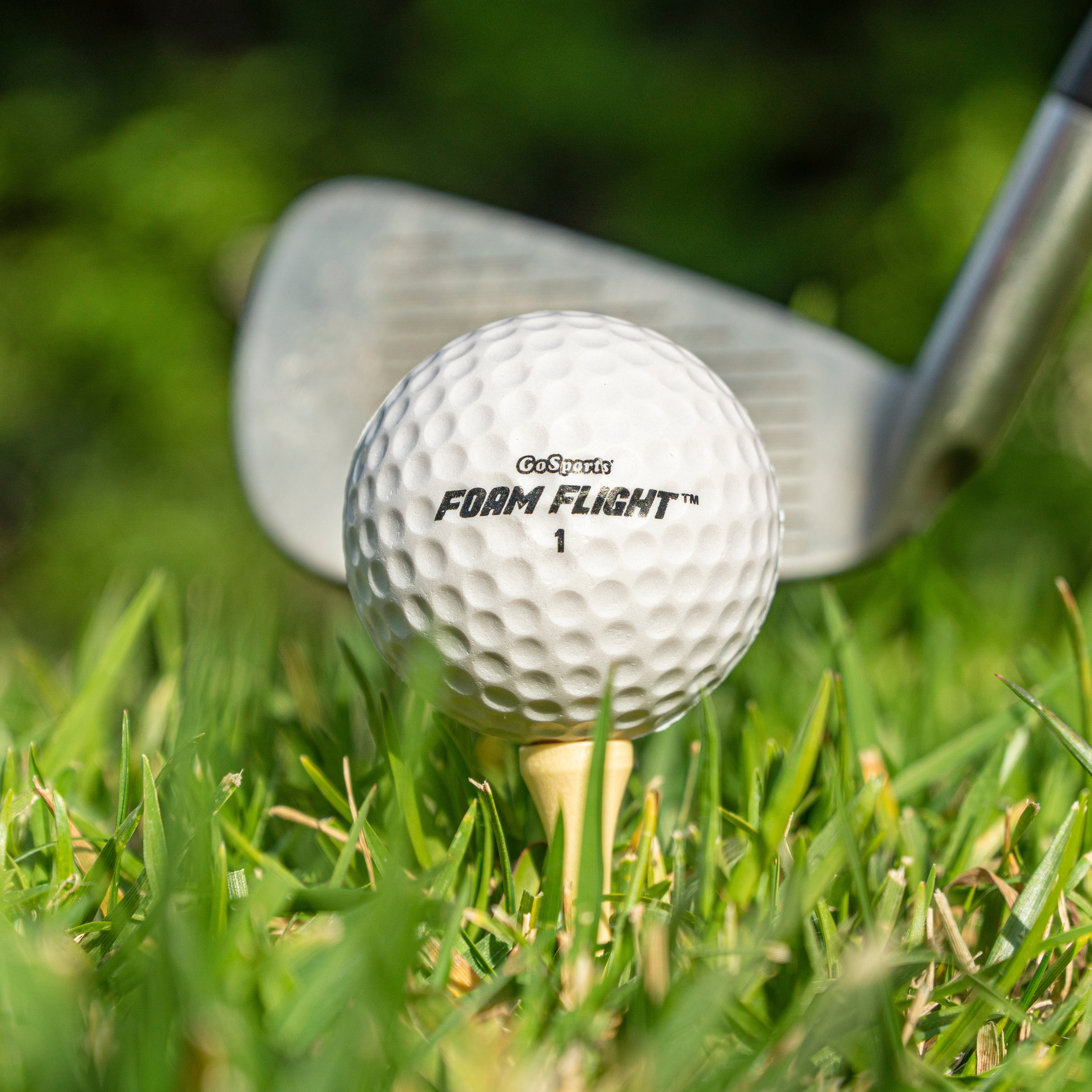 Golf ball on a tee with a golf club in the background on grass