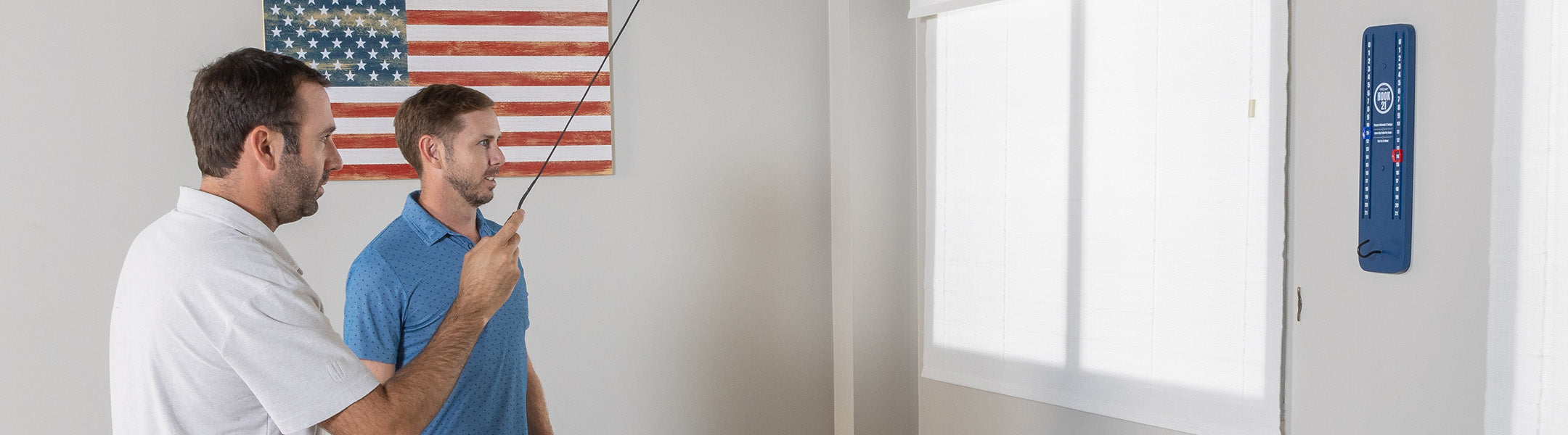 Two men in a room with an American flag on the wall and blue HOOK 21 game on the wall.