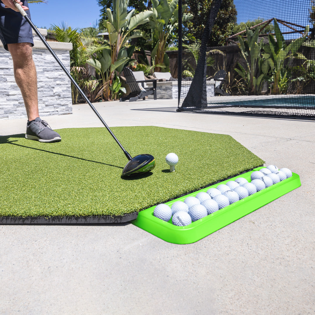 Person practicing golf swings on a mat with a ball holder full of golf balls.