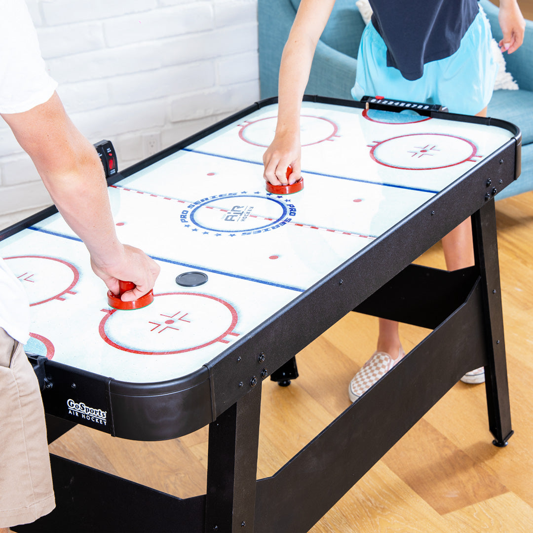 Two people playing air hockey on a table with red pucks.
