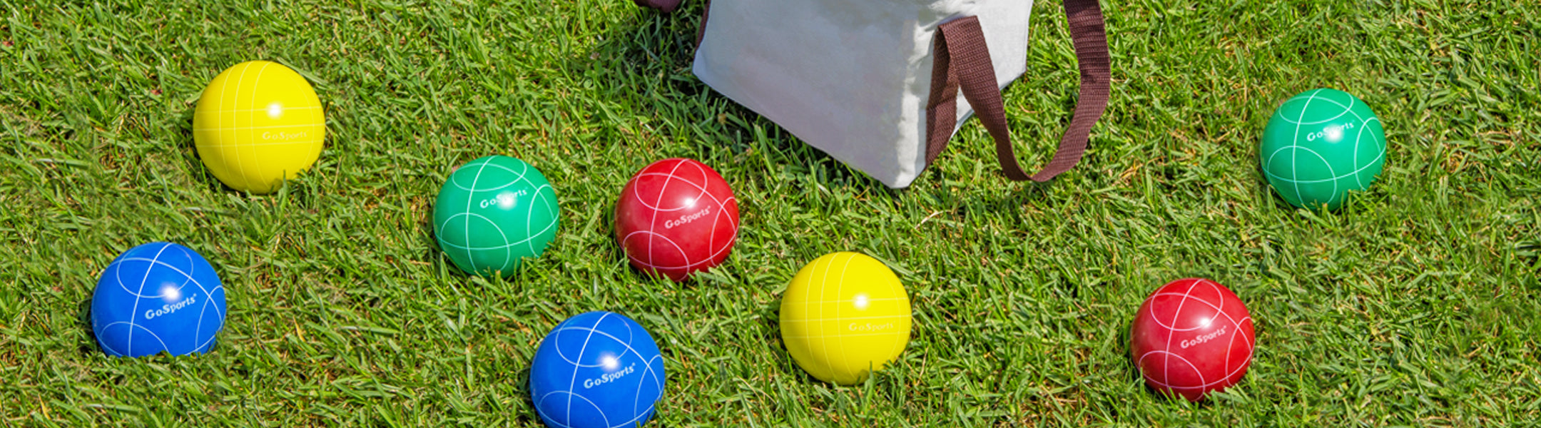 Colorful bocce balls on grass with a white bag in the background