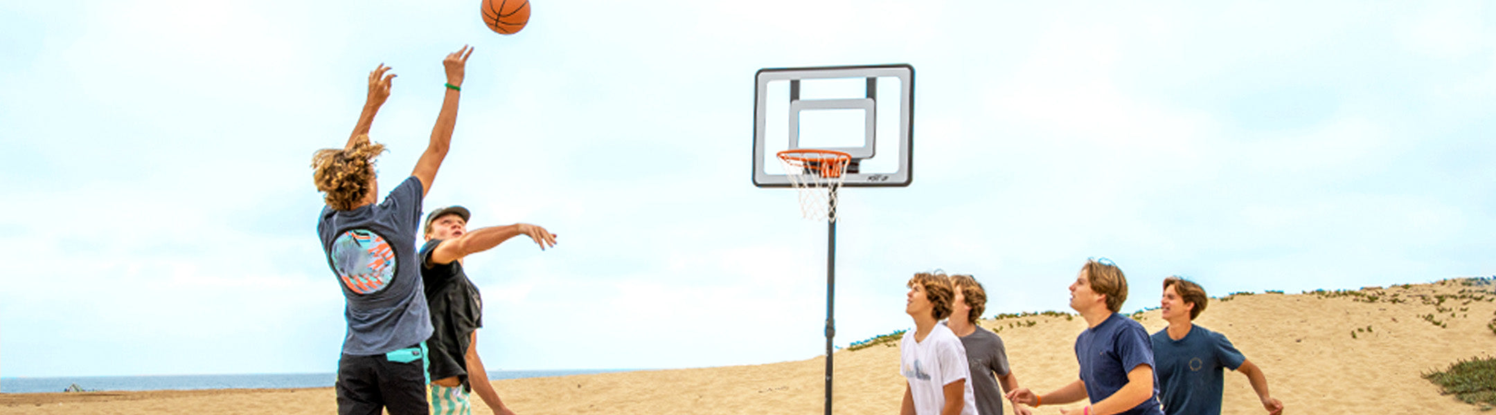 Group of people playing basketball on a beach with a clear sky.