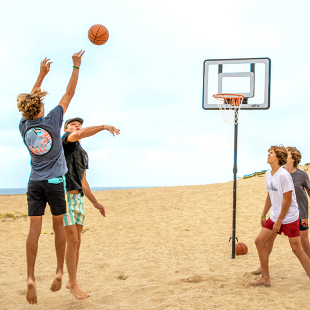 Children playing basketball on a sandy beach with a clear sky.
