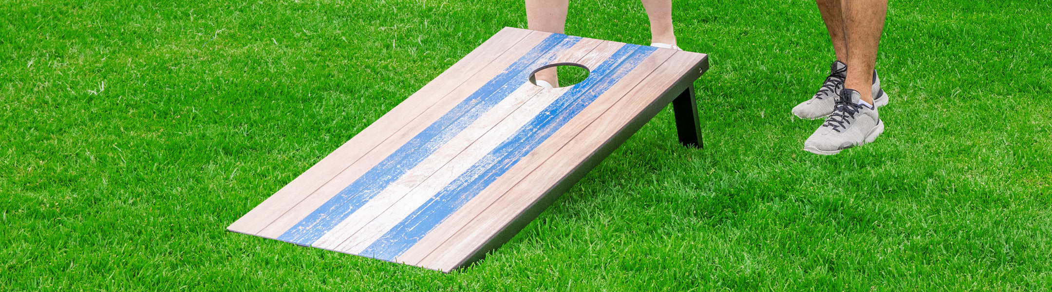 Cornhole board with blue and white stripes on a grassy field
