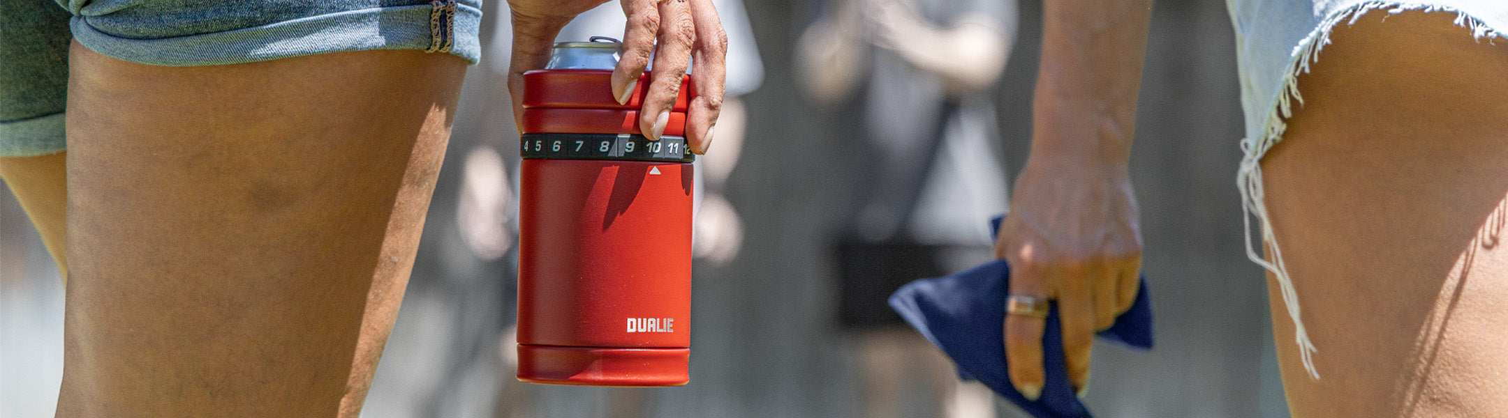 Two people holding red Dualie cup and blue bean bag with a blurred background