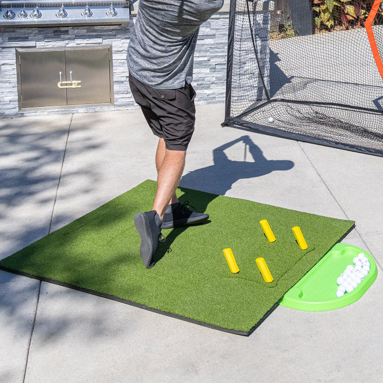 Person practicing golf swings on a mat with a golf net in the background
