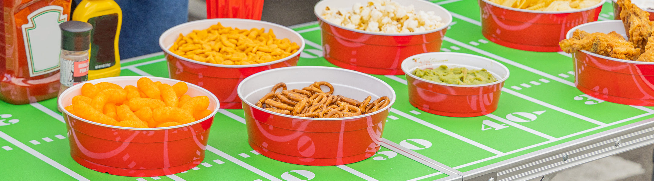 Assorted snacks in red bowls on a football-themed tablecloth