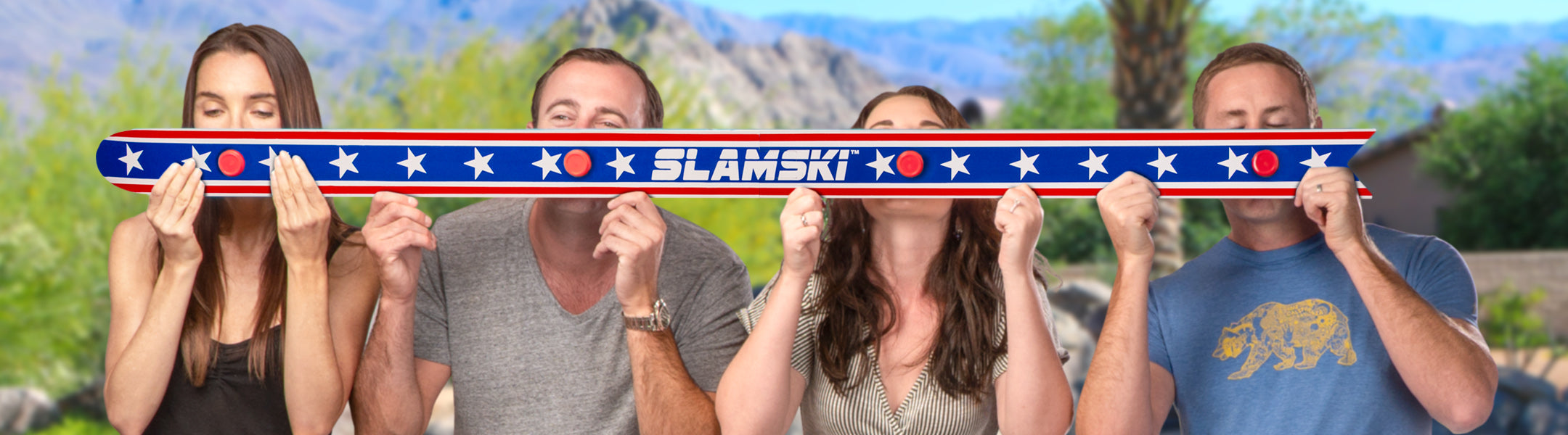 Four people holding a long, colorful object with 'Slamski' branding against a scenic background.