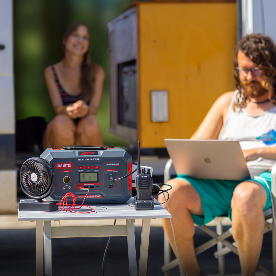 Person using a laptop with a power station on a table in an outdoor setting.