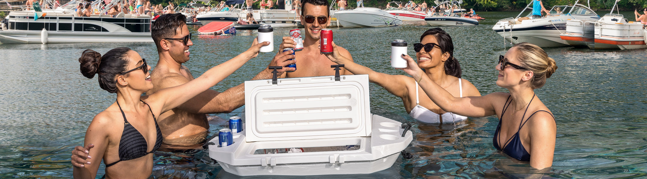 Group of people with a white cooler on a lake with boats in the background