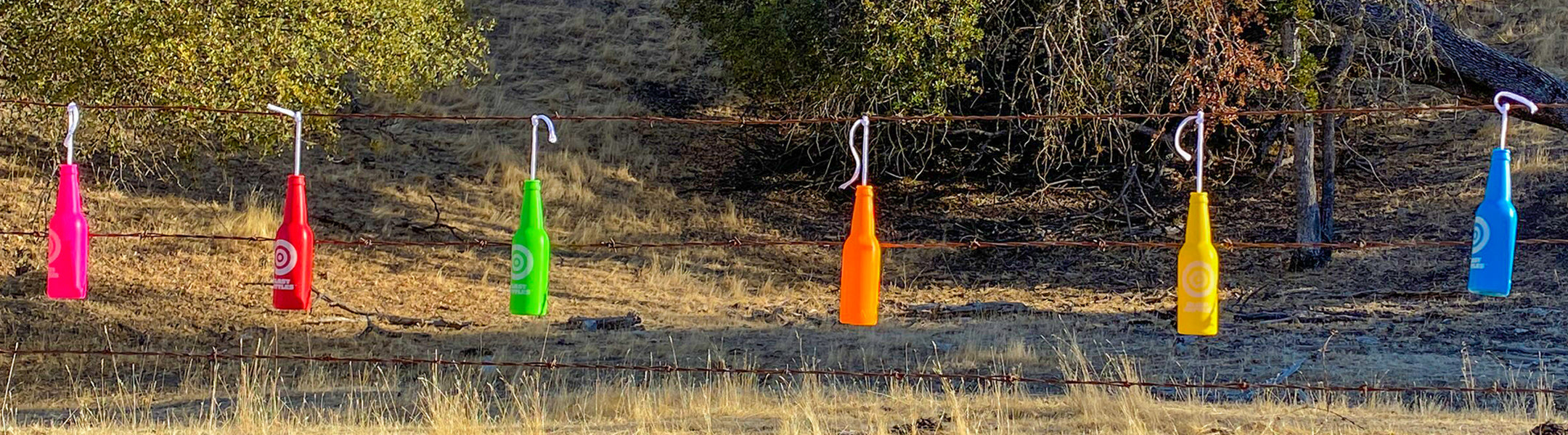 Colorful plastic bags hanging on hooks against a natural background with trees and grass.