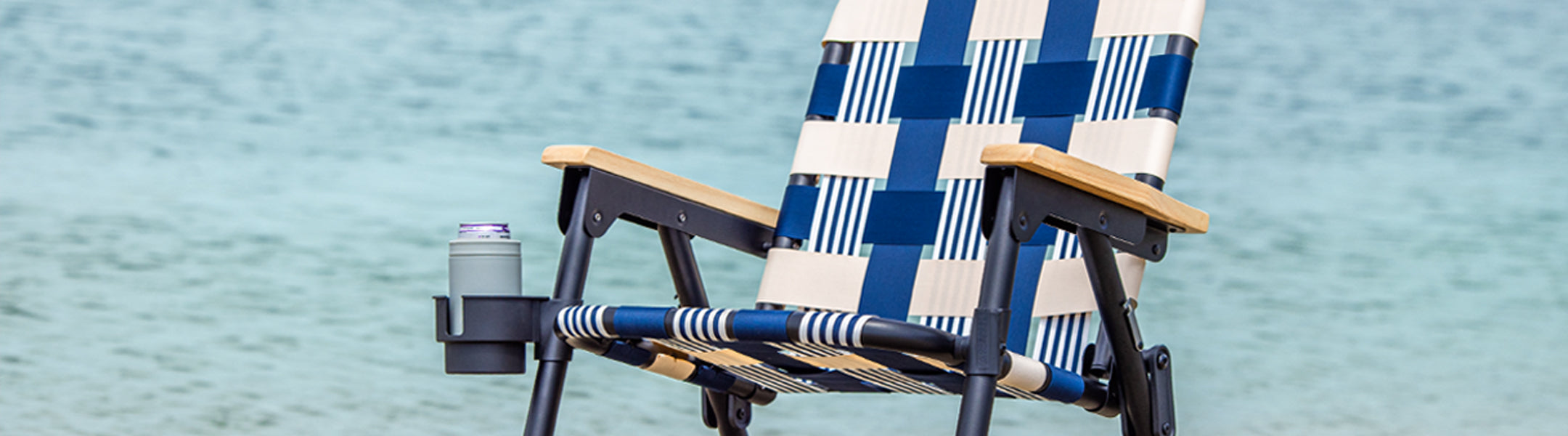 Blue and white checkered folding chair with a cup holder against a blurred water background