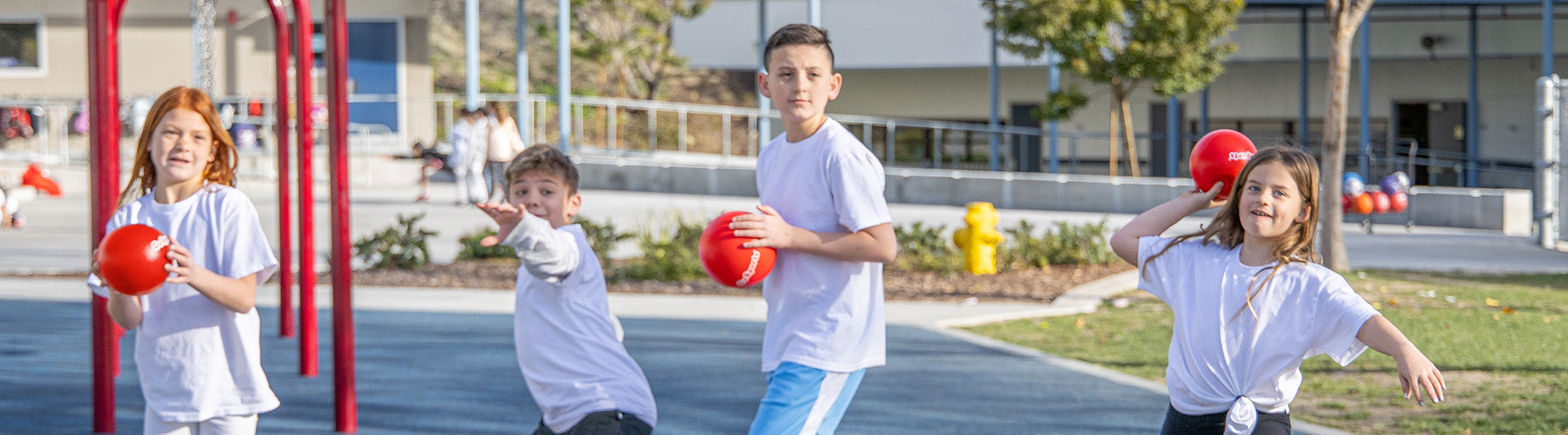 Four children playing with red balls on a playground.