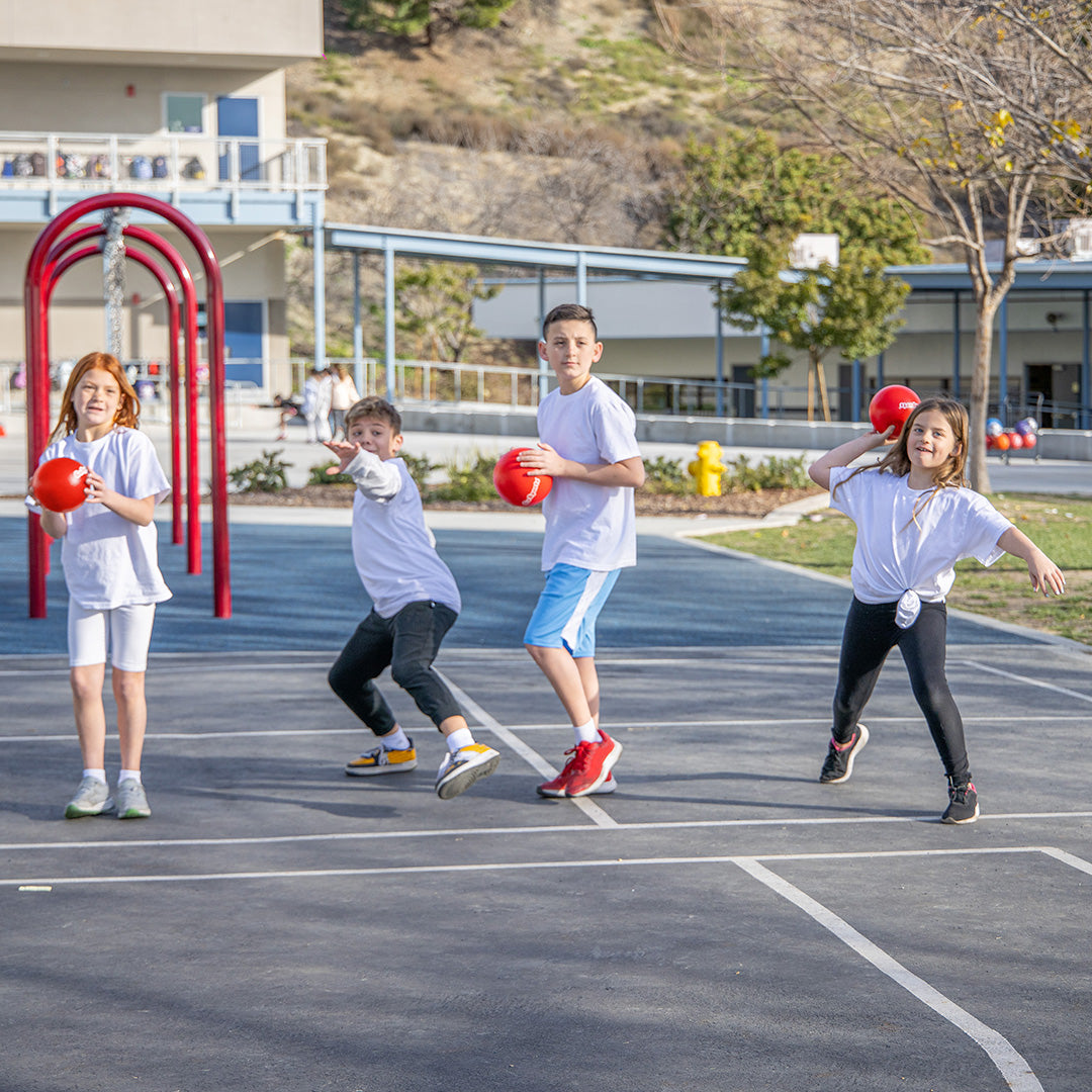 Four children playing with red balls on a school playground.