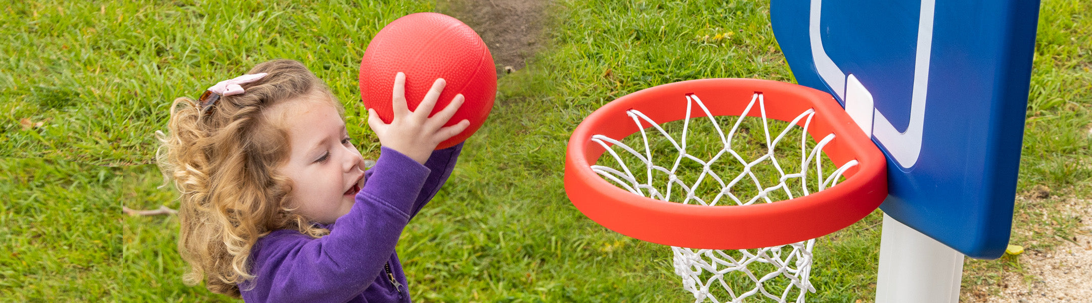 Child playing with a red basketball and hoop on grass