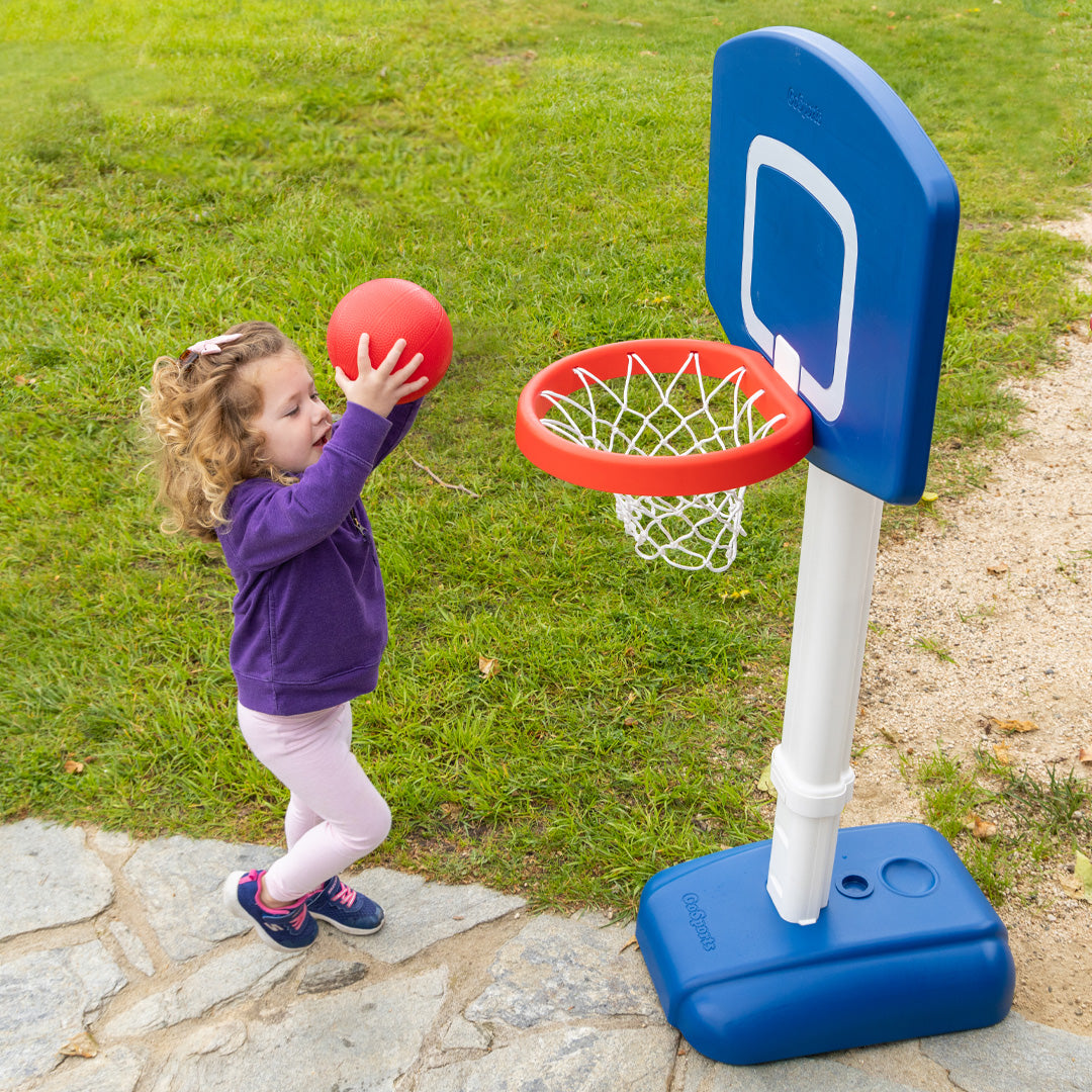 Child playing with a small basketball hoop and ball on a grassy area.