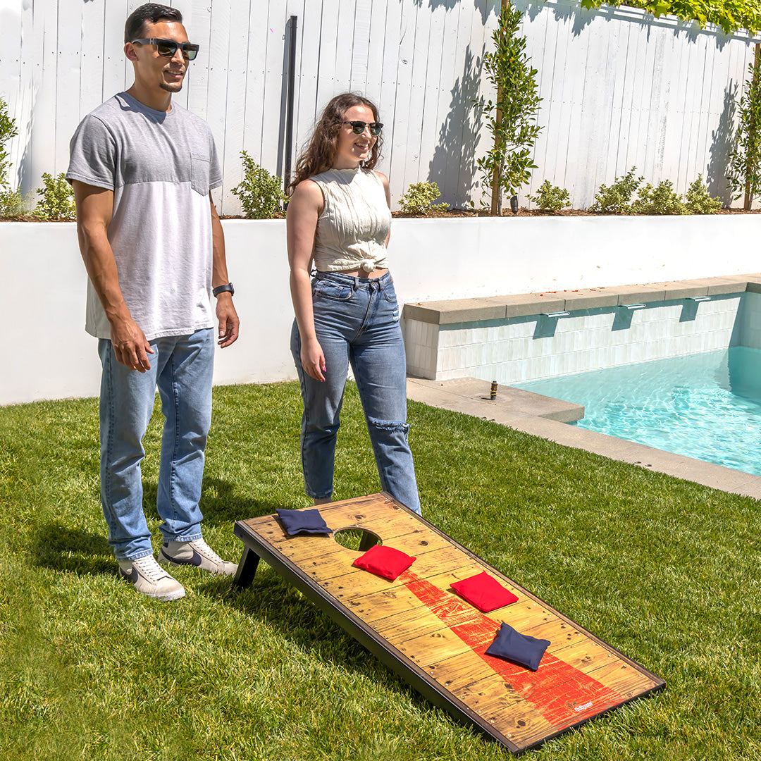 Two people playing cornhole by a pool