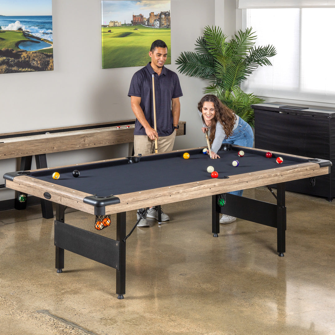 Two people playing pool in a room with a wall art and a plant.