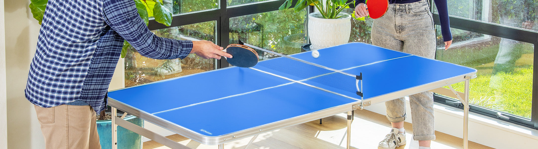 Two people playing table tennis on a blue table with a blurred indoor background