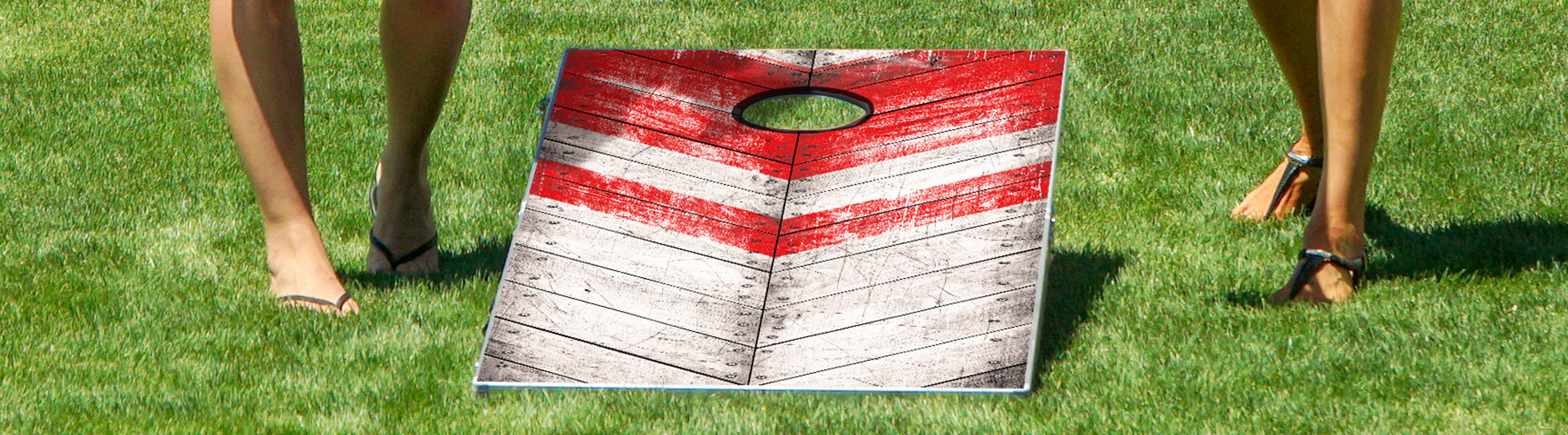Wooden cornhole board with red and white stripes on a grassy field