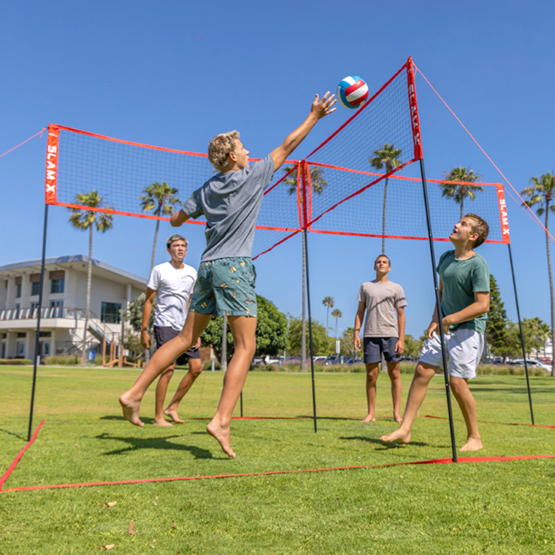Four people playing volleyball on a grassy field with a clear blue sky and palm trees in the background.