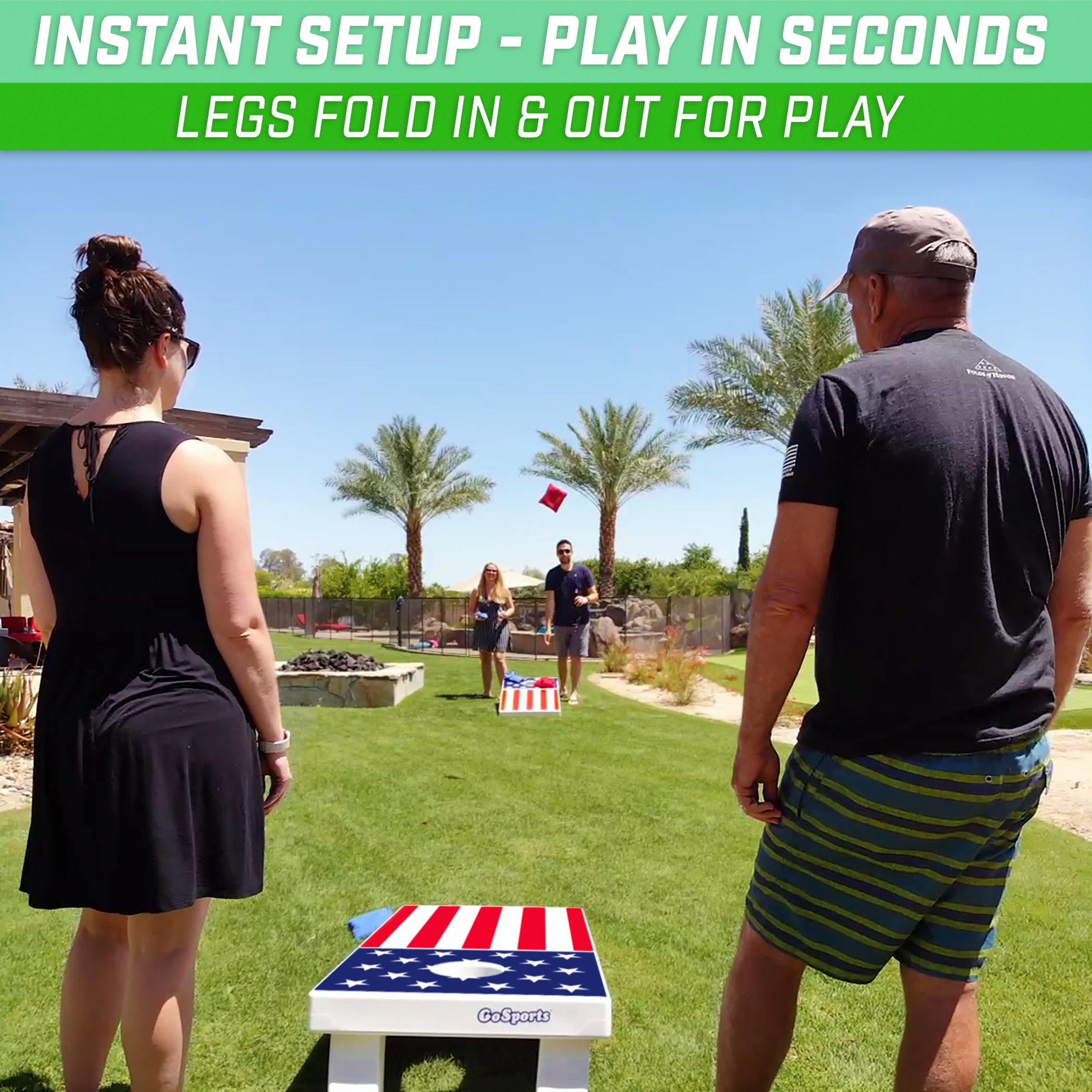 Man and woman standing next to an American flag design cornhole board. Across another man and woman throwing a red cornhole bag, outside on a green grass. 